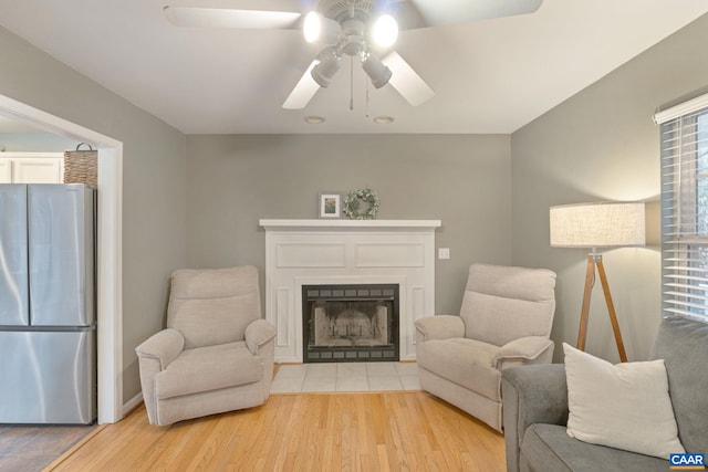 living area with a fireplace with flush hearth, ceiling fan, and light wood-style flooring