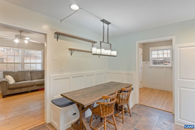 dining area featuring a ceiling fan, wainscoting, a decorative wall, and wood finished floors