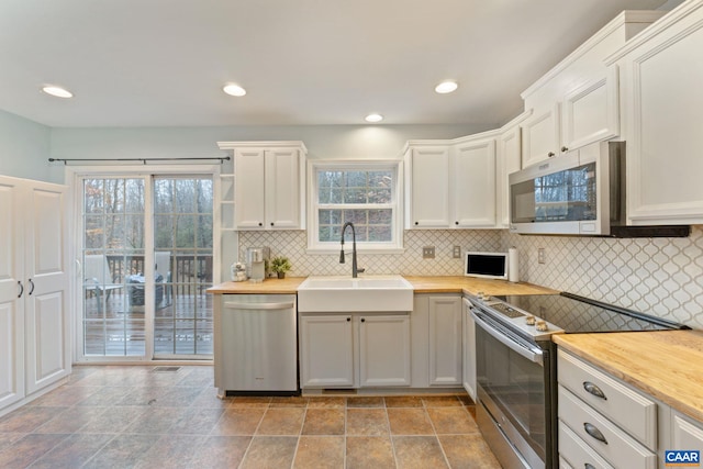 kitchen with stainless steel appliances, butcher block counters, white cabinetry, and a sink