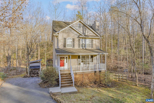 view of front of house with gravel driveway, a shingled roof, a chimney, and a porch