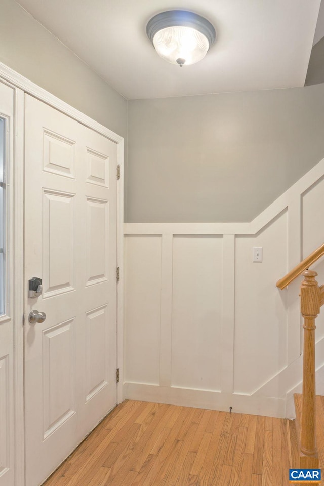 foyer entrance featuring light wood-style floors, stairway, wainscoting, and a decorative wall