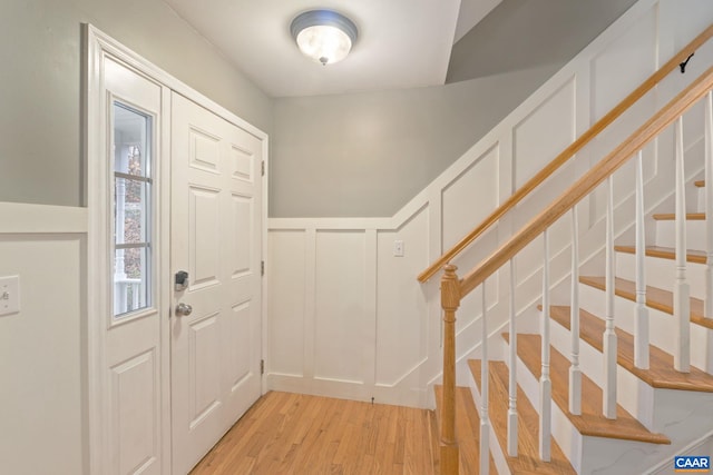 foyer with a wainscoted wall, light wood-style floors, stairway, and a decorative wall