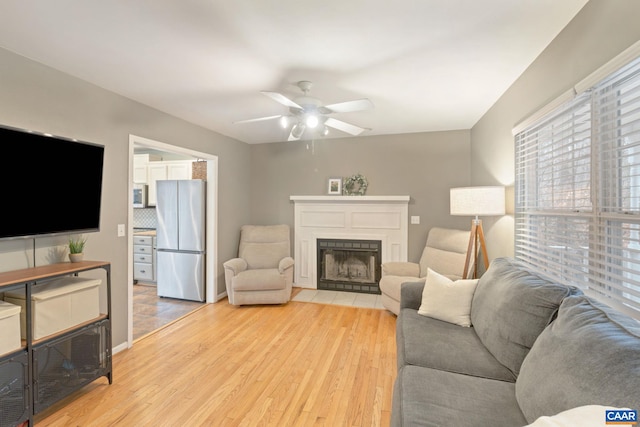 living area featuring ceiling fan, a fireplace, and light wood-style flooring