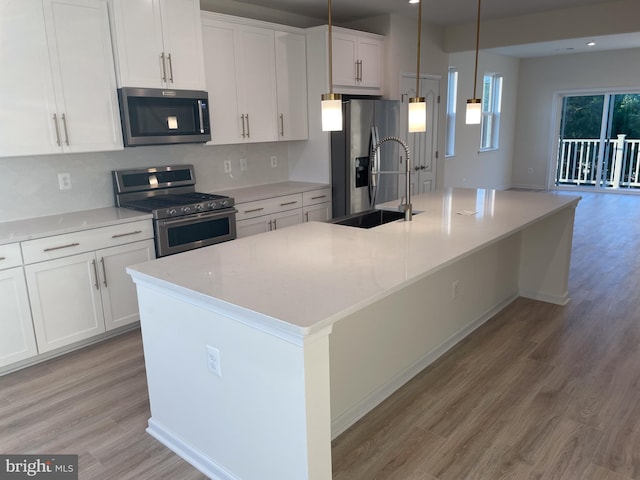 kitchen featuring a center island with sink, stainless steel appliances, hanging light fixtures, white cabinets, and a sink