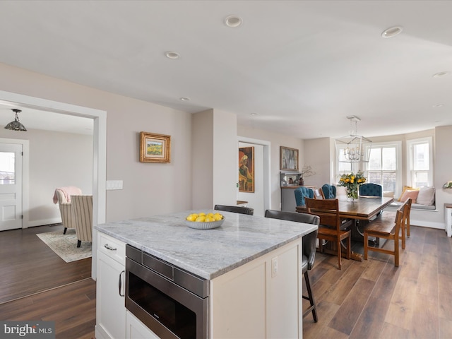 kitchen featuring a breakfast bar area, white cabinets, a center island, stainless steel microwave, and dark wood finished floors