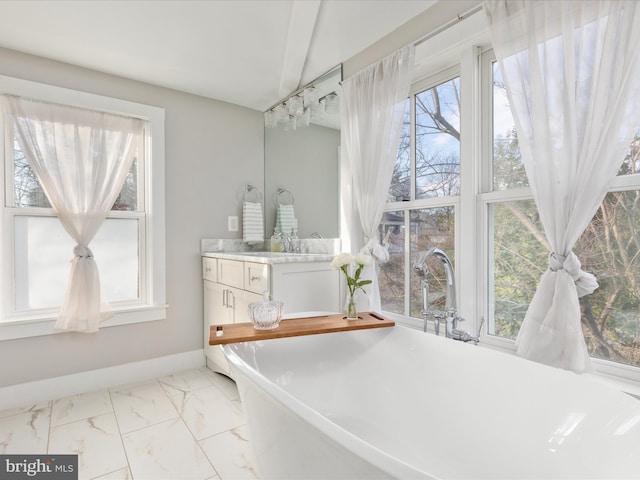 full bath featuring marble finish floor, a freestanding tub, vanity, and baseboards