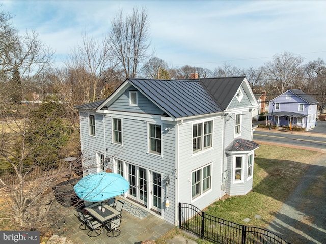 back of property featuring fence private yard, a standing seam roof, a chimney, and metal roof