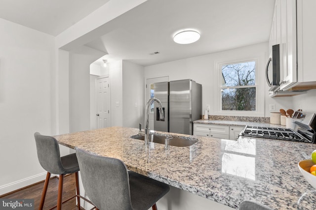 kitchen with appliances with stainless steel finishes, a kitchen breakfast bar, light stone countertops, white cabinetry, and a sink