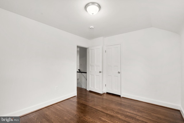 unfurnished bedroom with lofted ceiling, dark wood-style flooring, and baseboards