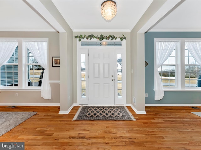 foyer featuring light wood-style floors, visible vents, crown molding, and baseboards