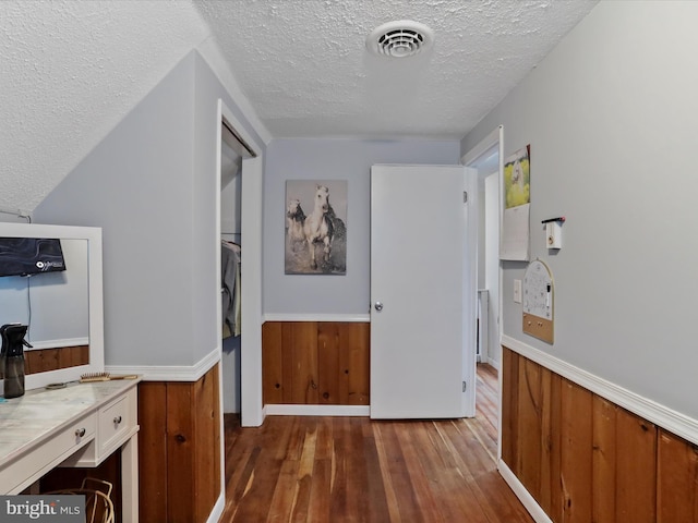 corridor with visible vents, dark wood-type flooring, a textured ceiling, and wainscoting