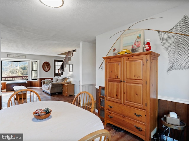 dining area featuring a textured ceiling, stairway, dark wood-style flooring, and wainscoting