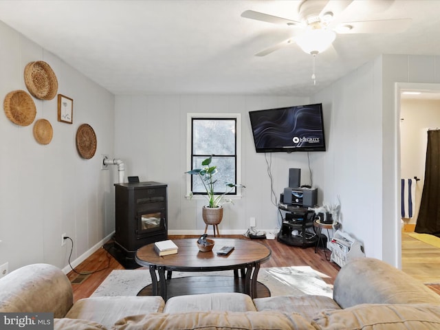 living area featuring ceiling fan, wood finished floors, a wood stove, and baseboards