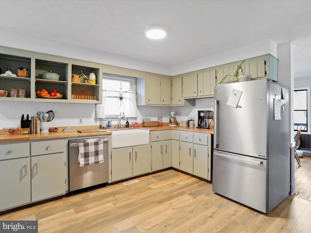 kitchen with light wood finished floors, open shelves, light countertops, appliances with stainless steel finishes, and a sink