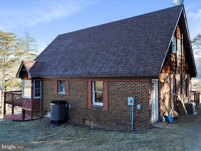 view of home's exterior with brick siding, a lawn, central AC unit, and roof with shingles