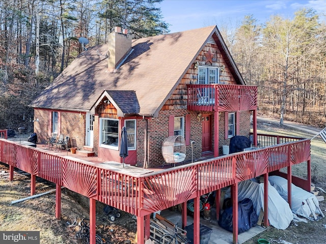 rear view of house featuring a deck, brick siding, a chimney, and roof with shingles