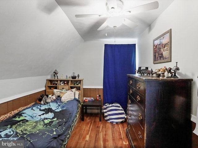 bedroom with a wainscoted wall, wooden walls, vaulted ceiling, and wood finished floors