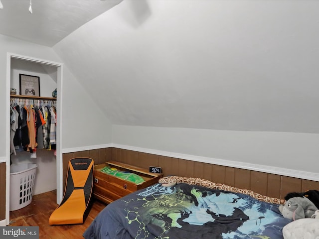 bedroom featuring lofted ceiling, a wainscoted wall, wood finished floors, wood walls, and a closet