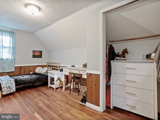 bedroom featuring a textured ceiling, wainscoting, lofted ceiling, and light wood-style flooring