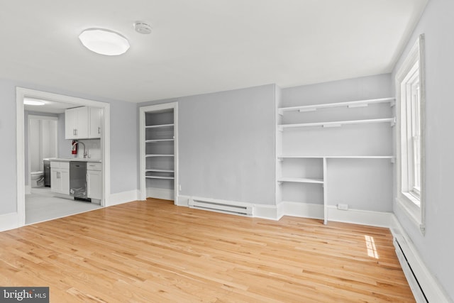 unfurnished living room with light wood-type flooring, a baseboard radiator, a sink, and baseboards