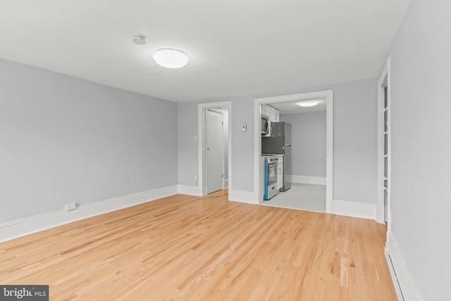 empty room featuring a baseboard heating unit, baseboards, and wood finished floors