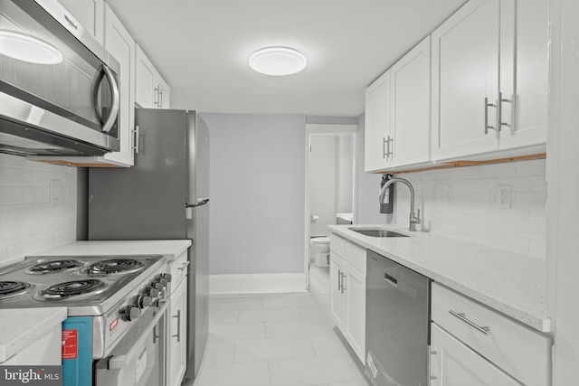 kitchen featuring light stone counters, stainless steel appliances, a sink, white cabinetry, and baseboards