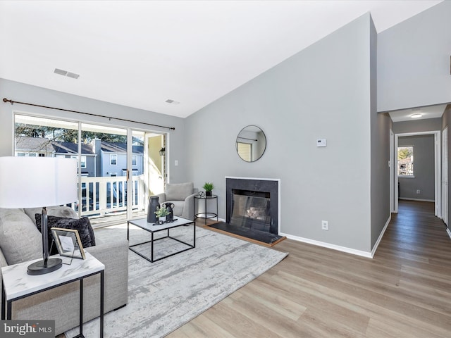 living room featuring baseboards, visible vents, a fireplace with raised hearth, wood finished floors, and high vaulted ceiling