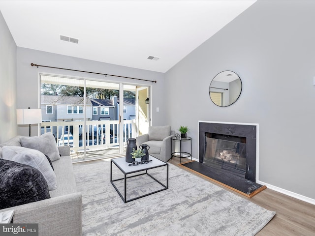 living area with lofted ceiling, visible vents, a fireplace with raised hearth, and wood finished floors