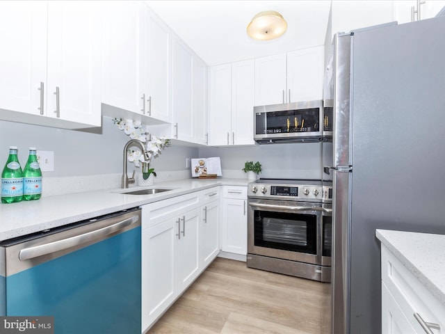 kitchen featuring light wood finished floors, light stone countertops, stainless steel appliances, white cabinetry, and a sink