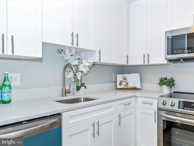 kitchen with stainless steel appliances, light stone counters, a sink, and white cabinets