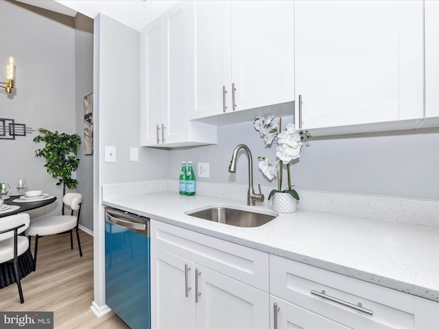 kitchen with light wood-style flooring, white cabinets, a sink, light stone countertops, and dishwasher