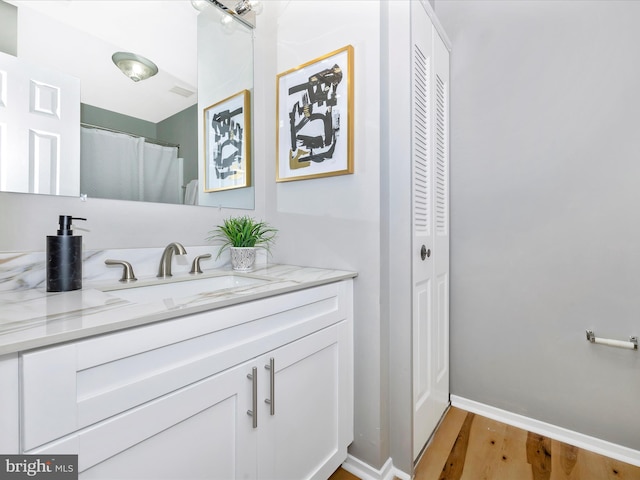 full bath featuring a closet, vanity, baseboards, and wood finished floors