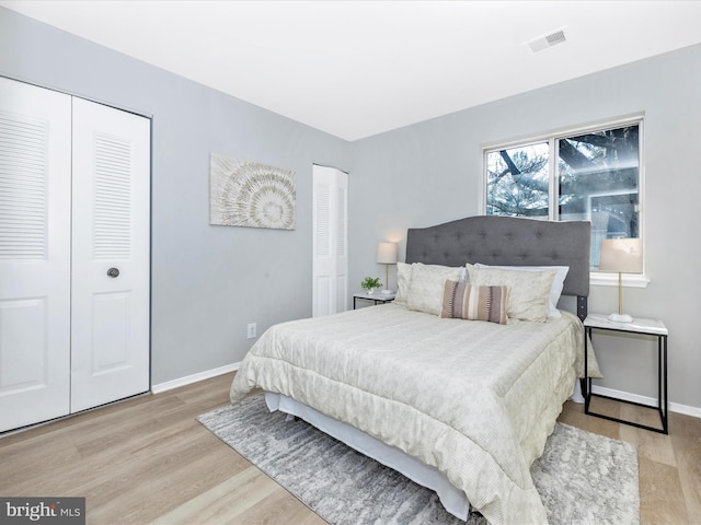 bedroom featuring light wood finished floors, two closets, visible vents, and baseboards