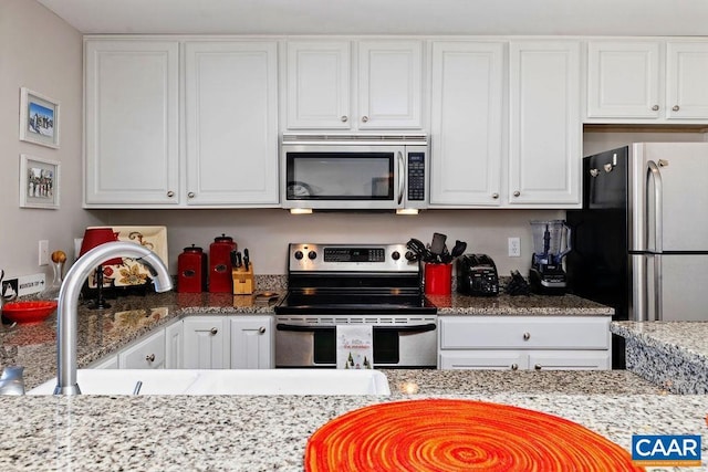 kitchen with stainless steel appliances, white cabinets, a sink, and light stone countertops