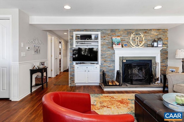 living area featuring a fireplace with raised hearth, dark wood-style flooring, wainscoting, and recessed lighting