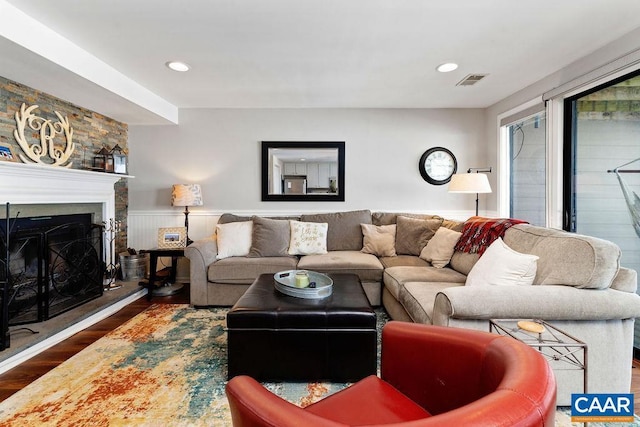 living area with a fireplace with raised hearth, recessed lighting, a wainscoted wall, visible vents, and dark wood-style floors