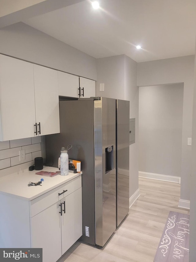 kitchen with stainless steel refrigerator with ice dispenser, light countertops, backsplash, light wood-style flooring, and white cabinetry