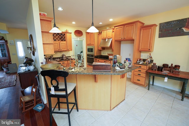 kitchen with pendant lighting, appliances with stainless steel finishes, under cabinet range hood, a peninsula, and a kitchen breakfast bar