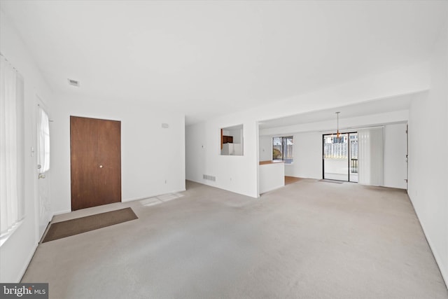 unfurnished living room featuring a chandelier, visible vents, and light colored carpet