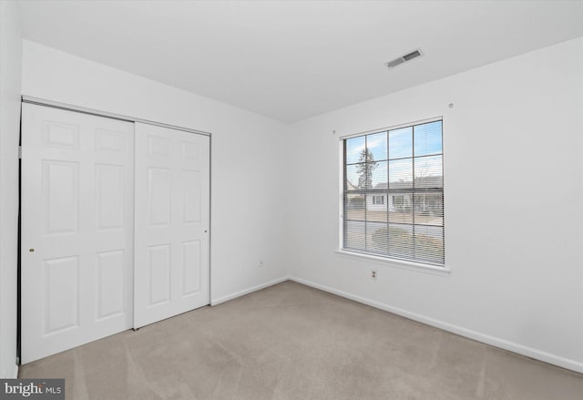 unfurnished bedroom with light carpet, a closet, visible vents, and baseboards