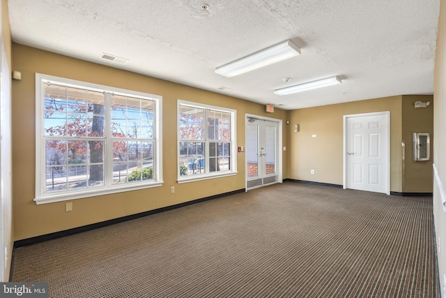 unfurnished room featuring visible vents, dark carpet, a textured ceiling, and baseboards