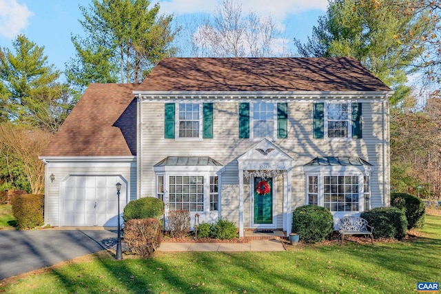 colonial inspired home featuring a garage, roof with shingles, aphalt driveway, and a front yard