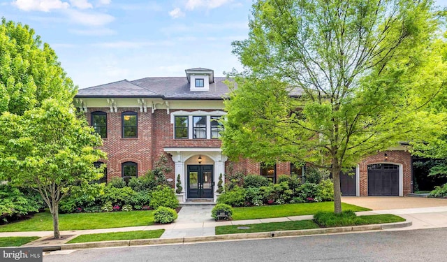 view of front facade featuring french doors, brick siding, a front yard, a garage, and driveway