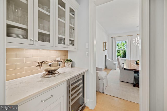 bar featuring light wood finished floors, wine cooler, ornamental molding, decorative light fixtures, and backsplash