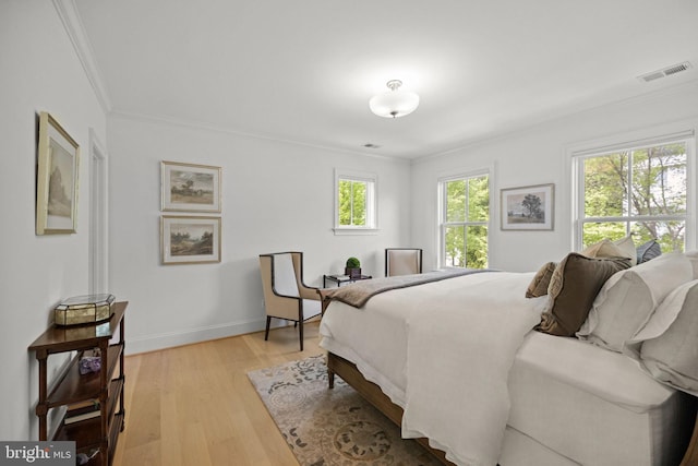 bedroom with baseboards, visible vents, crown molding, and light wood finished floors