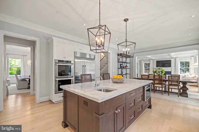 kitchen with light stone counters, hanging light fixtures, appliances with stainless steel finishes, white cabinets, and a sink