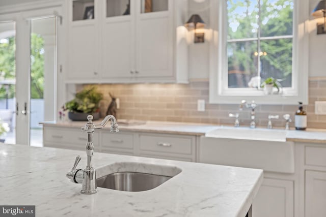 kitchen with white cabinets, glass insert cabinets, light stone counters, and a sink