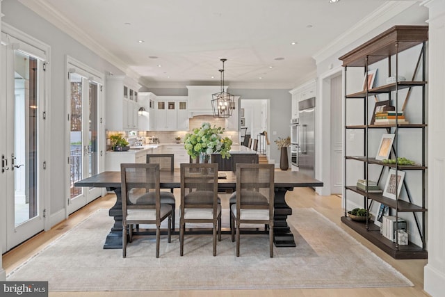 dining area featuring ornamental molding, french doors, light wood-style flooring, and an inviting chandelier