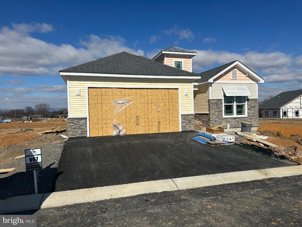 view of front of house with driveway, stone siding, an attached garage, and roof with shingles