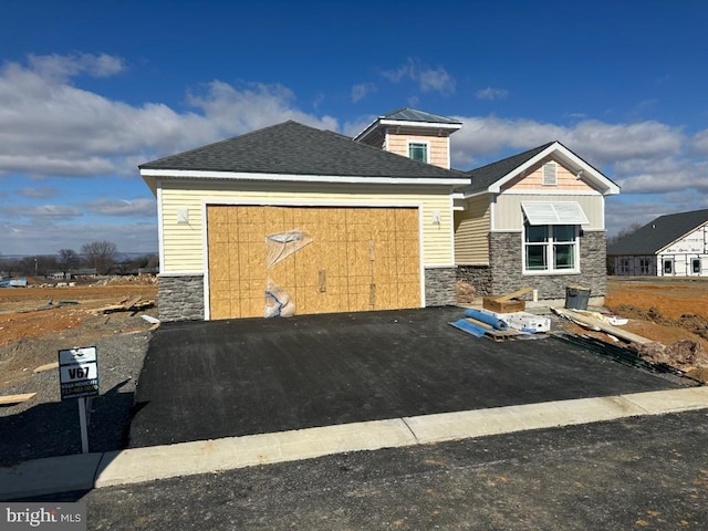 view of front of house with driveway, stone siding, an attached garage, and roof with shingles